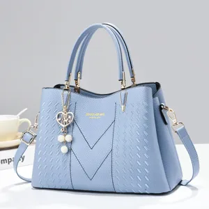 Blue leather handbag close-up showing V-stitch details, top handles and pearl heart charm.