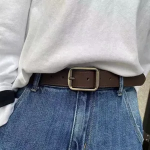 Close-up detail of retro brown leather belt with matte silver square buckle on blue jeans.