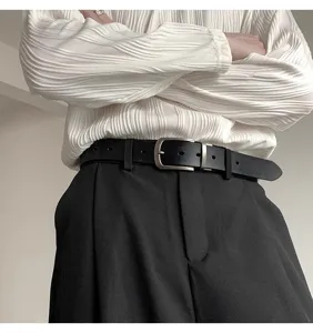 Close-up of a classic black leather belt with a sleek silver pin buckle, worn on trousers.