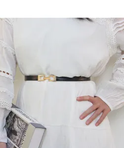 Vue rapprochée d'une fine ceinture noire minimaliste à boucle rectangulaire dorée sur robe.