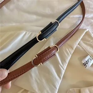 Detailopname van dunne PU lederen riem in zwart en bruin met stijlvolle metalen gesp.