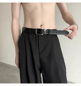 Men's black leather belt detail shot featuring a classic metal pin buckle and sleek black trousers.