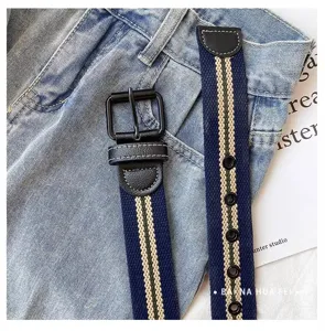 Detail view of women canvas belt with metal buckle, blue striped casual jeans waistband.