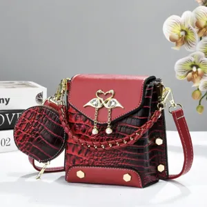 Détail exquis du sac bandoulière en croco rouge, avec charme de cygne en perle et porte-monnaie.