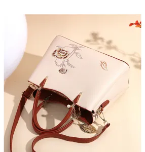 Elegant beige women handbag with Chinese embroidery, brown handles and trendy leaf charm.