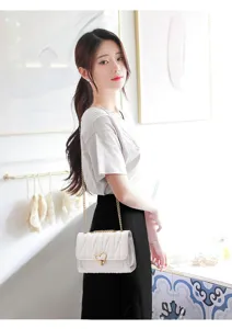 Detail view of a white quilted shoulder bag featuring a sweet heart lock and gold chain strap.