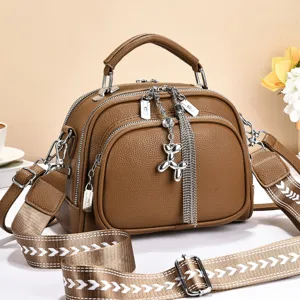 Stylish brown women crossbody bag featuring a wide strap, multiple pockets and a metal charm.