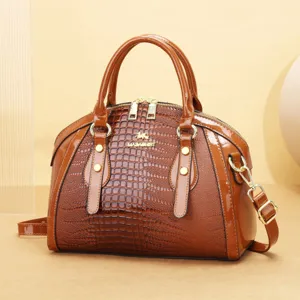 Détail de sac à main en cuir verni marron avec texture croco gaufrée et quincaillerie dorée.
