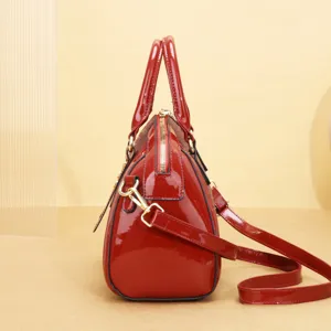 Vue rapprochée du détail latéral du sac à main en cuir verni rouge avec monogramme et métal doré.
