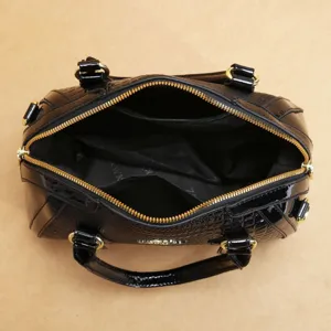 Sac à main en cuir vernis noir avec quincaillerie dorée et compartiment intérieur spacieux.