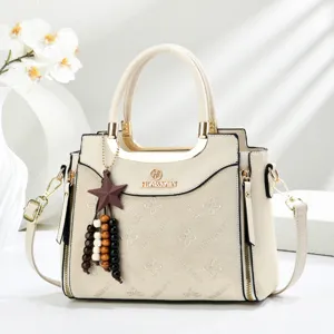 Chic beige handbag detail view featuring elegant metal handle, charm, and branded embossed design.