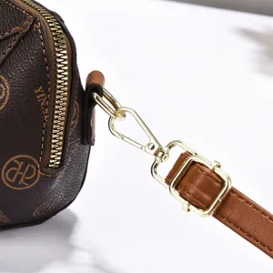 Close-up detail of women's brown monogram crossbody bag strap and golden metal hardware.
