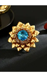 Elegante gouden zonnebloem broche met lichtblauwe kristal en kleurrijke strass details.