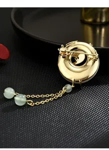Close-up detail of the vintage gold-colored metal brooch back with green bead tassel chains.