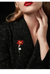 Detailed close-up of an elegant red lily flower brooch with pearl pendant and crystal accents.