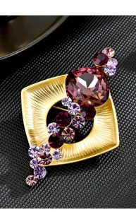 Elegante broche geométrico dorado con cristales violetas, accesorio perfecto para traje.