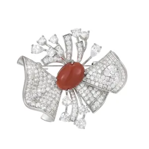 Élégante broche nœud avec oxydes de zirconium pavés et pierre centrale rouge.