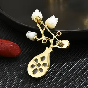Vintage gold-plated vase brooch with white shell flowers and red gemstone accents, elegant.