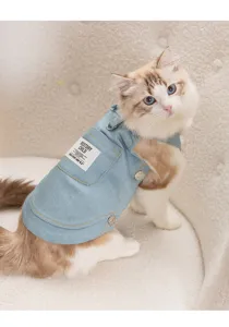 Close-up detail of cute cat wearing a light blue denim pet vest with decorative pocket.