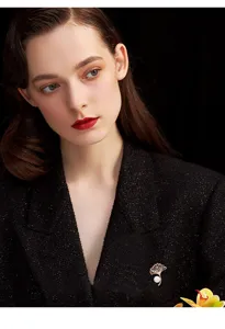Detailed shot of elegant ginkgo leaf brooch with pearls and crystals on dark coat fabric.