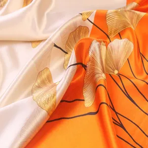 Close-up detail of luxurious satin square scarf with vibrant orange botanical print.