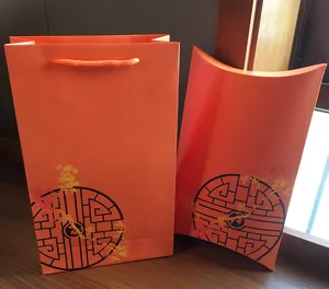 Orange paper gift bag and pillow box packaging set with traditional Chinese pattern details.