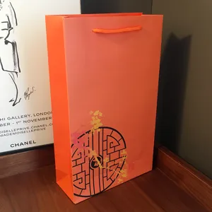 Orange paper gift bag with handles and traditional circular pattern for holiday presents.