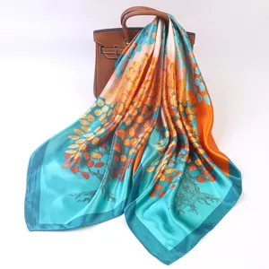 Silk square scarf detail showing glossy satin fabric texture, vibrant tree leaf print pattern.