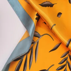 Close-up view of a yellow silk satin scarf detail showing leaf pattern and blue-grey border.