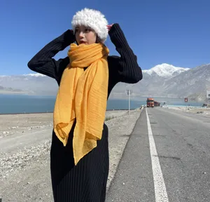 Outdoor detail shot of a bright yellow long cotton linen scarf worn by a model near a scenic road.