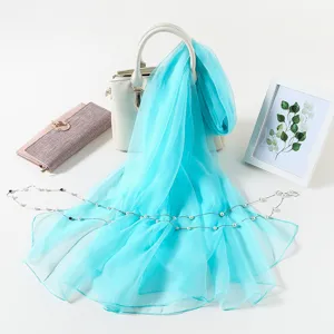 Detailed view of lightweight turquoise chiffon scarf draped on white handbag in clean styling.