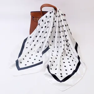 Detailed view of elegant black and white polka dot square silk scarf draped on a bag.
