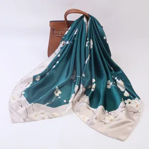 Elegant dark green silk square scarf with floral print draped on luxury leather handbag