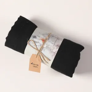 Detailed view of rolled black cotton linen scarf with elegant printed paper packaging band.