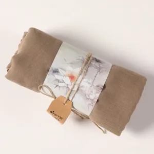 Detailed close-up shot of a rolled khaki cotton linen scarf wrapped with lotus art paper and tag.