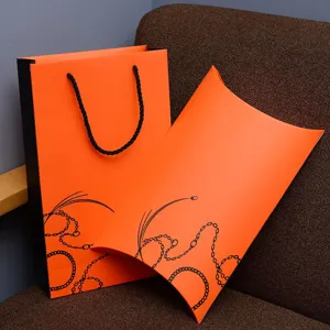 Close-up detail of orange gift packaging boxes and bag with black chain patterns.