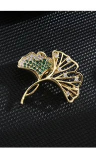 Elegant double ginkgo leaf brooch detail, featuring green and white zirconia in gold finish.