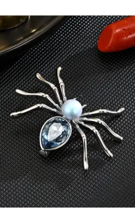 Detaillierte Nahaufnahme der eleganten silbernen Spinnenbrosche mit hellblauem Kristall und Perle.