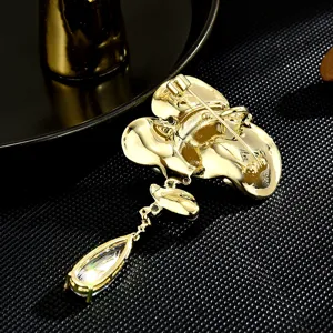 Gold tone lotus brooch with teardrop crystal pendant, elegant suit coat pin accessory for women.