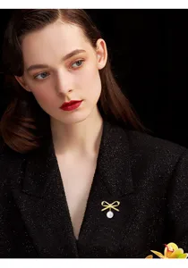Close-up detail showing elegant gold bow pearl brooch pinned on black tweed jacket lapel.