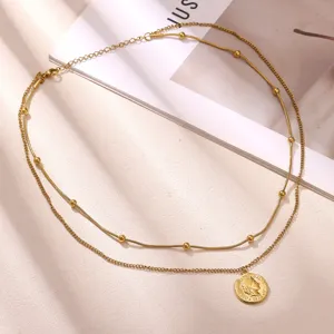 Gros plan d'un collier étagé en acier inoxydable doré avec perles et pendentif pièce.