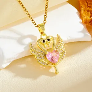 Close-up detail of a gold-plated twin swan pendant necklace with sparkling pink heart crystal.