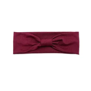Dettaglio in primo piano della fascia per capelli a fiocco in maglia a costine bordeaux.