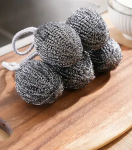 Detail shot of stainless steel wire mesh cleaning ball with lanyard on wooden board scene.
