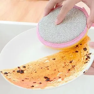 Double-sided cleaning sponge detail showing effective oil removal on dirty kitchen plates.