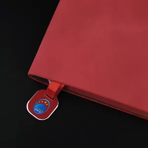 Red leather notebook with ribbon bookmark and custom pendant for office and business use.