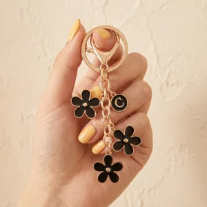 Gold keychain featuring black enamel flower charms and initial letter C pendant for bags and keys.