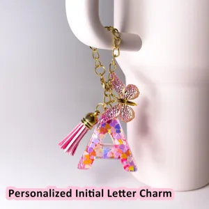 Ciondolo lettera in resina con farfalla rosa e nappa, perfetto per decorare chiavi e borse.