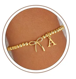 Gold beaded bow letter bracelet detail showing refined charm and elegant wrist wear.