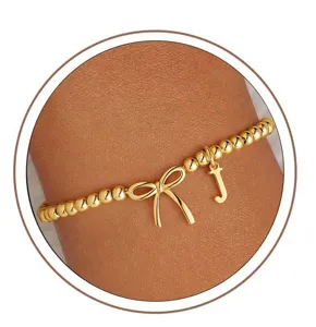 Gold beaded stretch bracelet detail featuring bow charm and letter J initial pendant.
